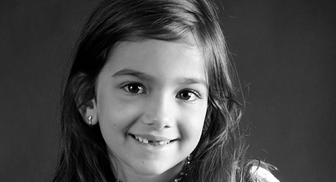 طفلة تتوسط الصورة، وعلى وجهها ابتسامة.