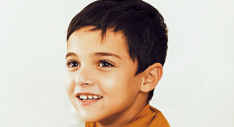 طفل يتوسط الصورة، يرتدي قميصاً باللون البرتقالي وعلى وجهه ابتسامة.
